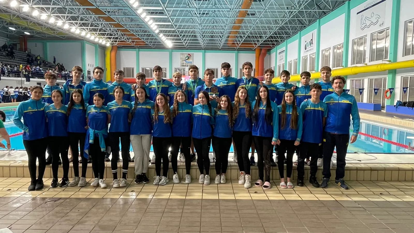 Equipo infantil y júnior del club con chándal azul, posando junto a la piscina cubierta