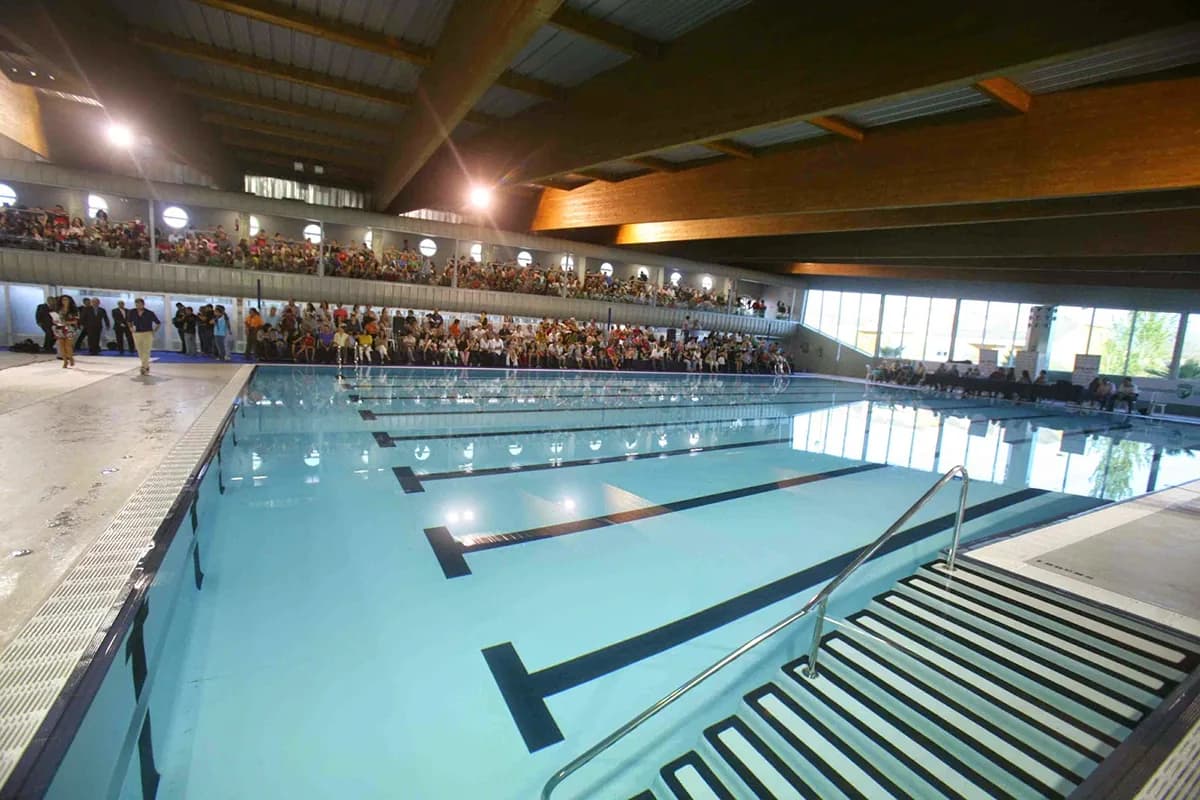 Piscina cubierta con las calles sin nadadores y público en la grada
